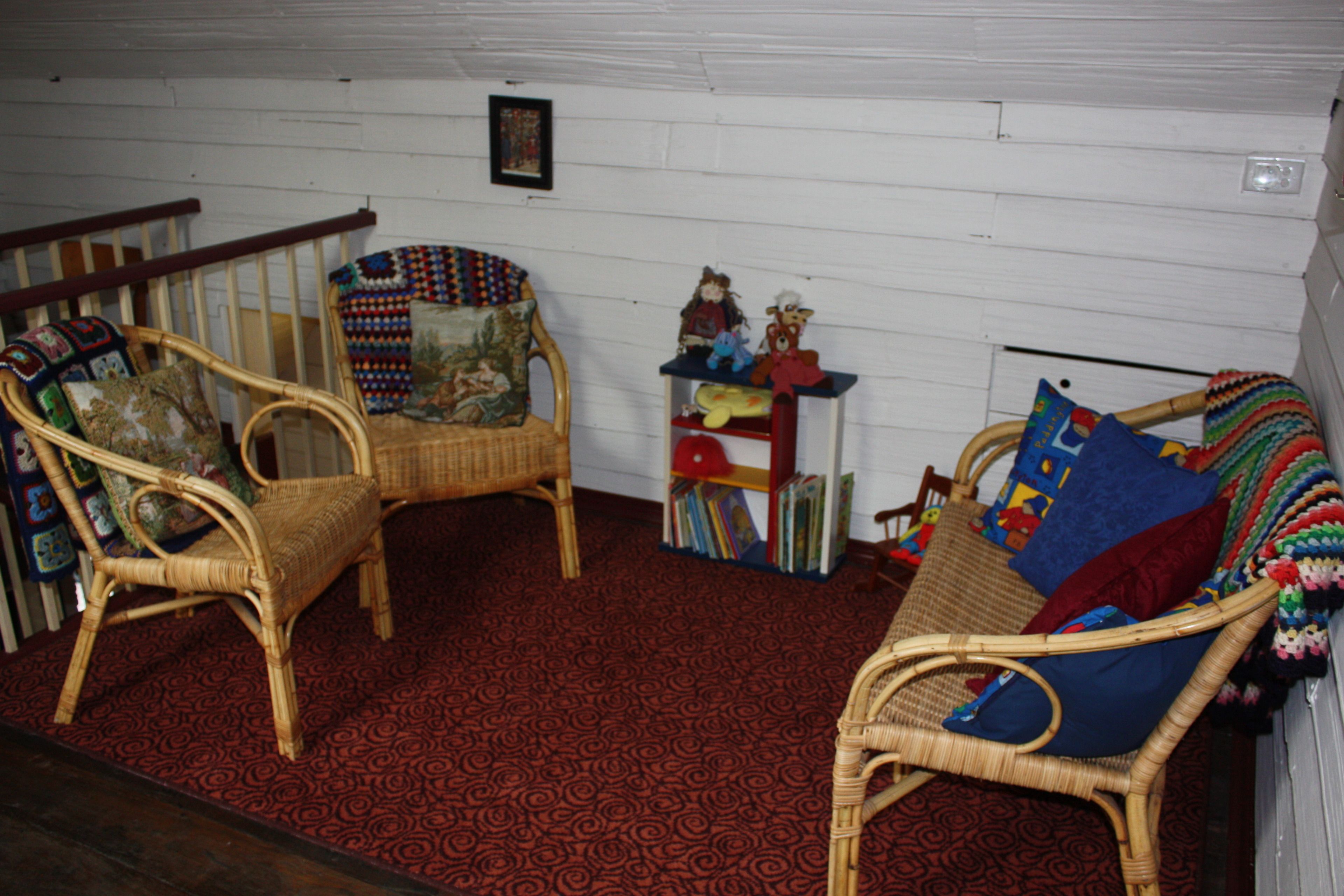 A room with two wicker chairs, a small table with books and toys, and a patterned carpet.