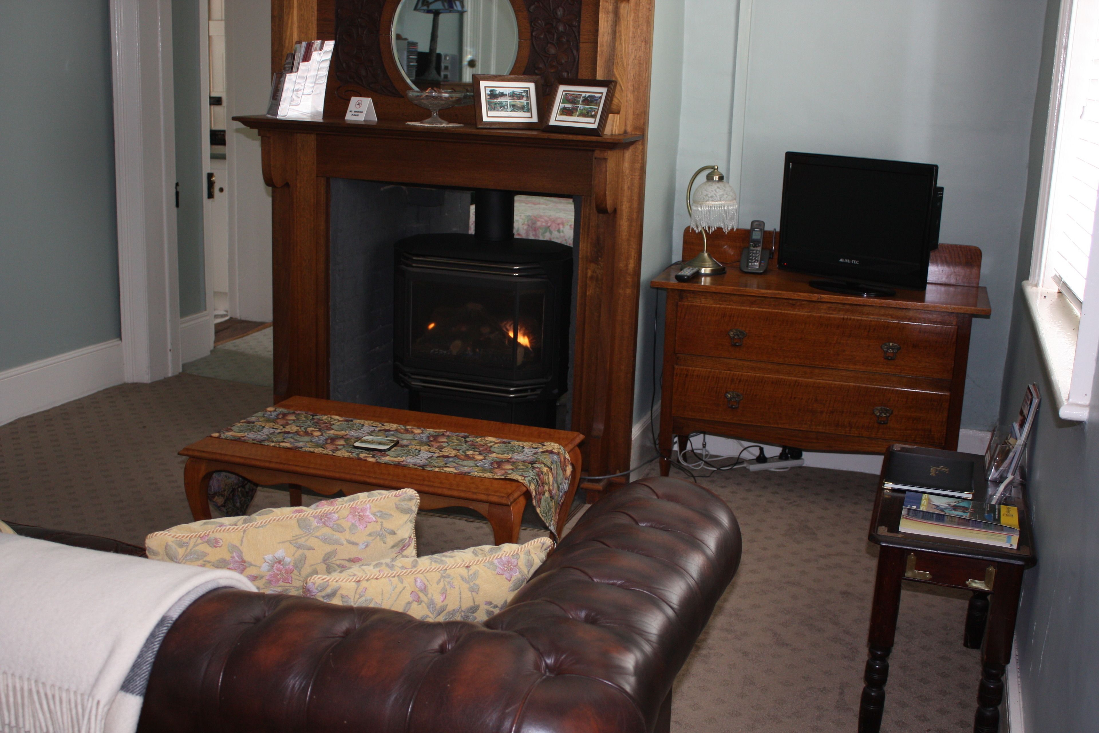 A cozy living room with a fireplace, a television on a wooden stand, a sofa, and a small table with a floral tablecloth.