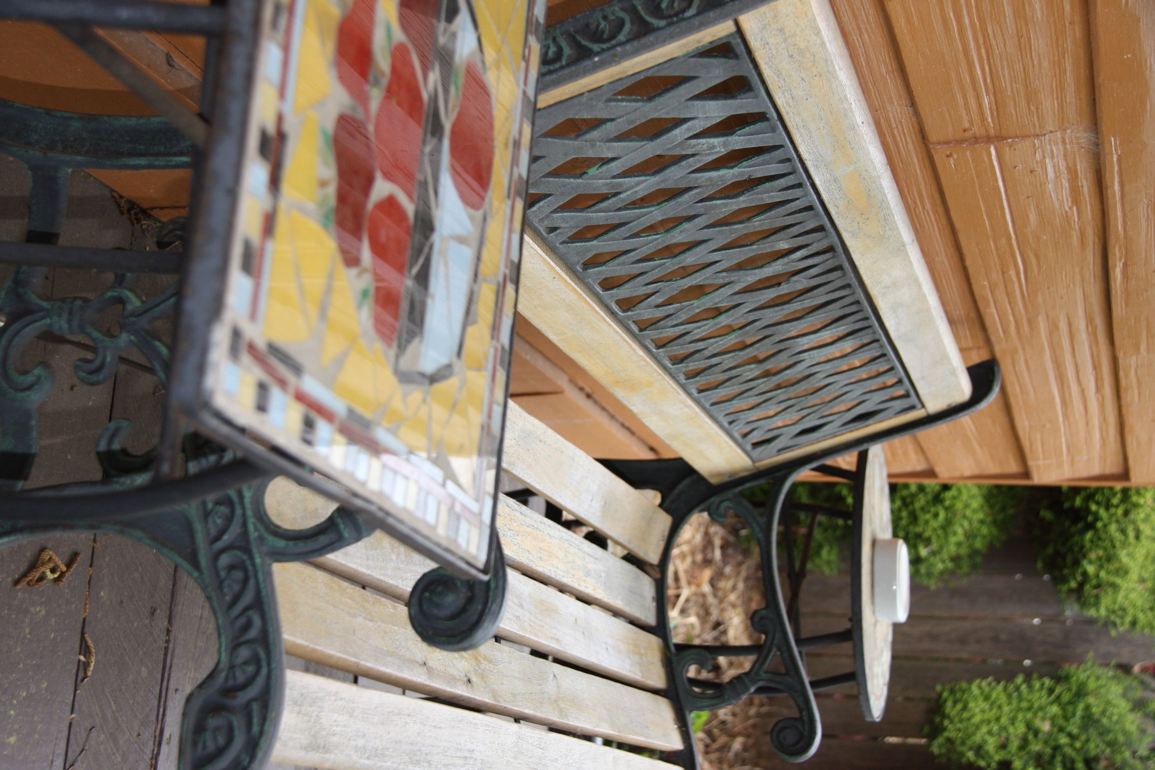 A wooden bench with metal backrests and a metal table with a patterned design.