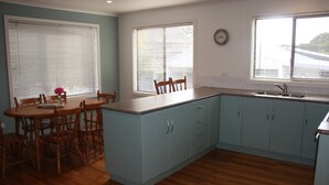 A kitchen with a dining area, wooden cabinets, a sink, and a clock on the wall.