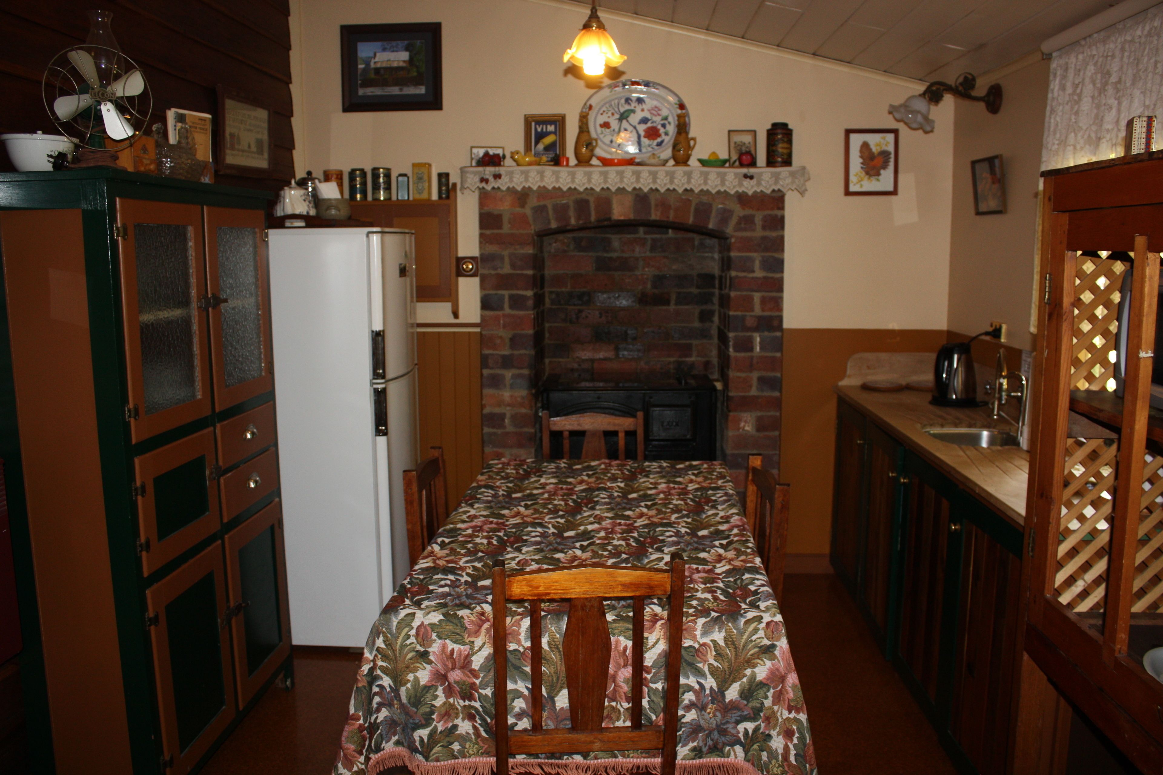 A dining area with a table set for two, a brick fireplace, and a kitchen area with a sink and cabinets.