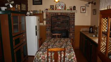 A dining area with a table set for two, a brick fireplace, and a kitchen area with a sink and cabinets.