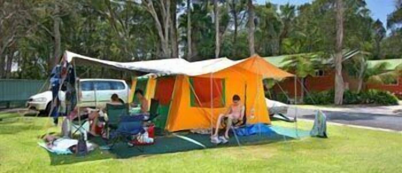 Un'area campeggio con una grande tenda arancione, una tenda blu più piccola e un veicolo bianco parcheggiato nelle vicinanze.
