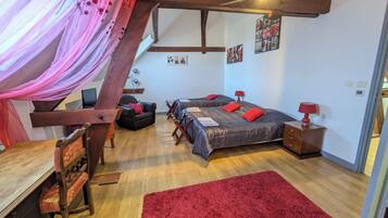 A cozy bedroom with a wooden ceiling, two beds with red pillows, a red rug, and a desk with a chair.