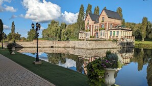 Een historisch gebouw met een symmetrische gevel, een stenen brug en een rustig waterlichaam dat de structuur weerspiegelt.