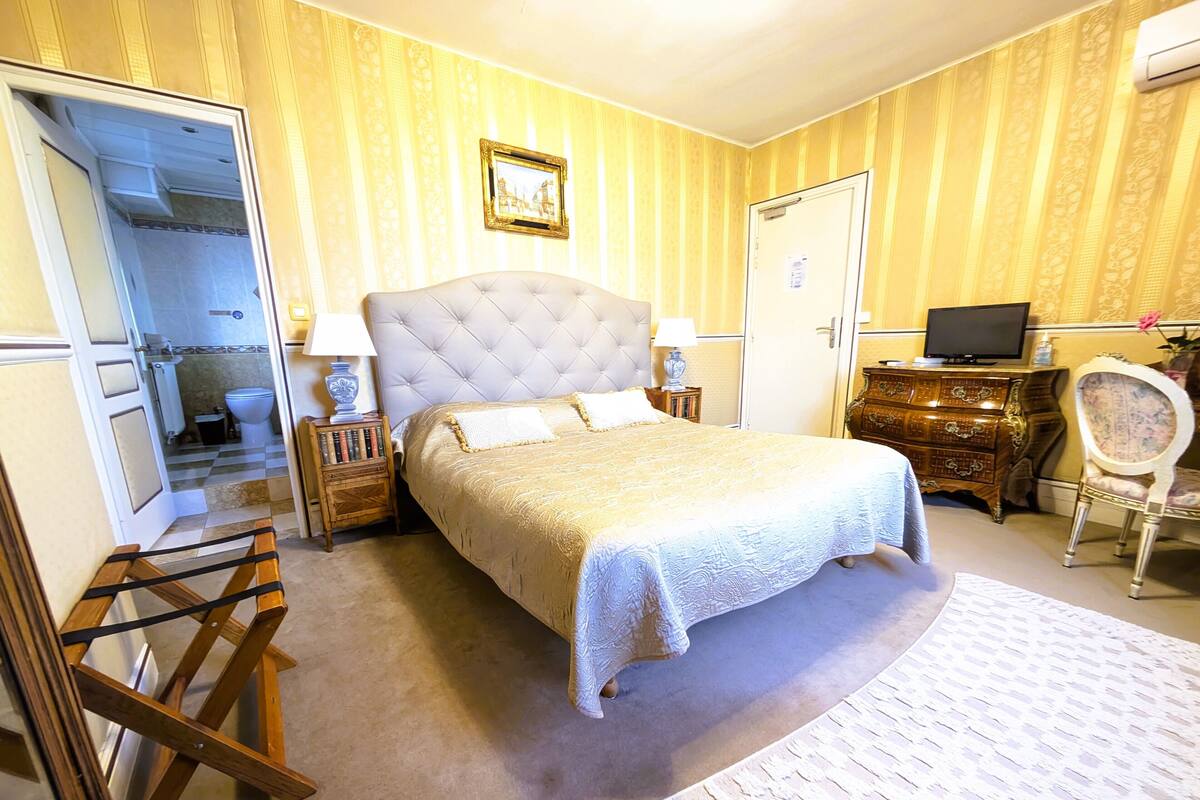Ein Schlafzimmer mit einem großen Bett, einem Holzschrank, einem Fernseher auf einer Kommode und einem Sessel.