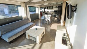 Een ruime woonkamer met een bank, salontafel en een eettafel met stoelen. In de achtergrond is een keuken te zien.