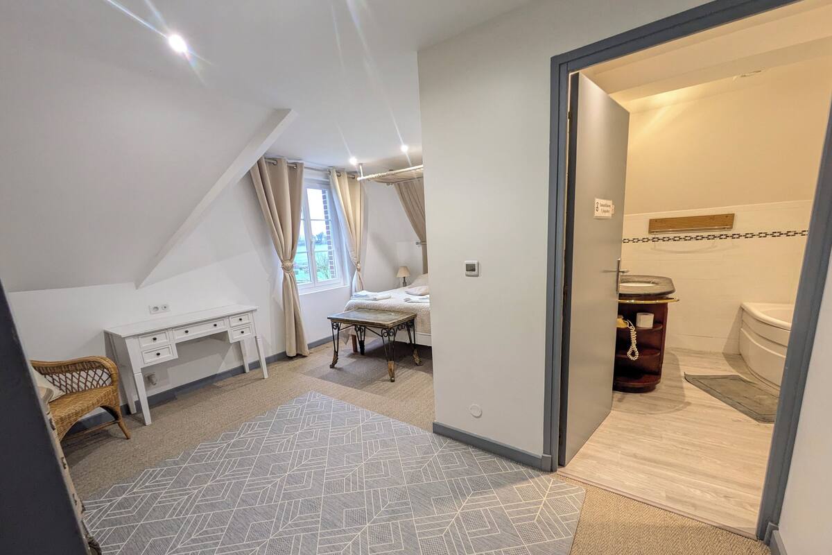 Ein Schlafzimmer mit einem Bett, einem Schreibtisch und einem Stuhl. Ein Badezimmer ist durch eine geöffnete Tür sichtbar.