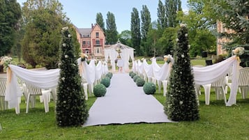 Un pasillo nupcial con cortinas blancas y follaje verde que conduce a un quiosco blanco.
