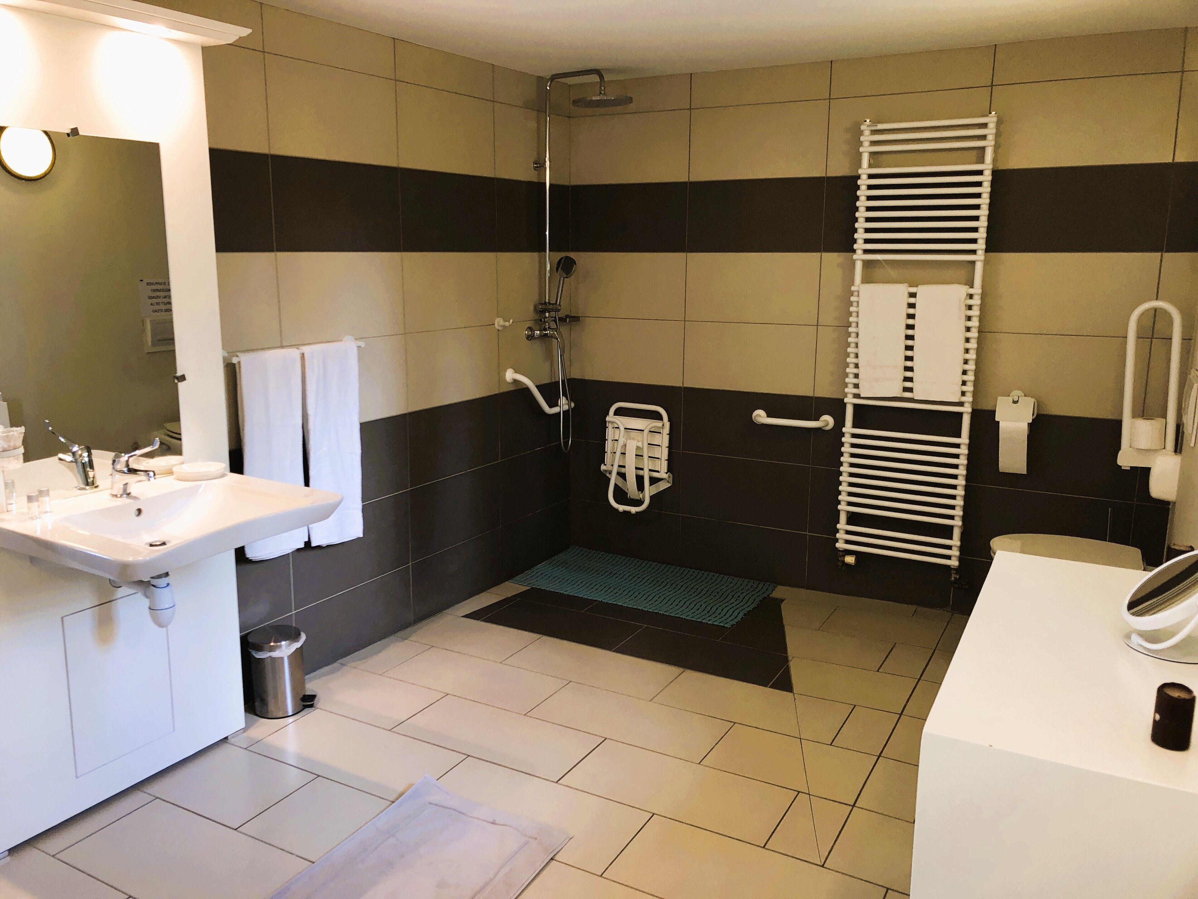 A bathroom with a sink, mirror, shower, and towel rack.