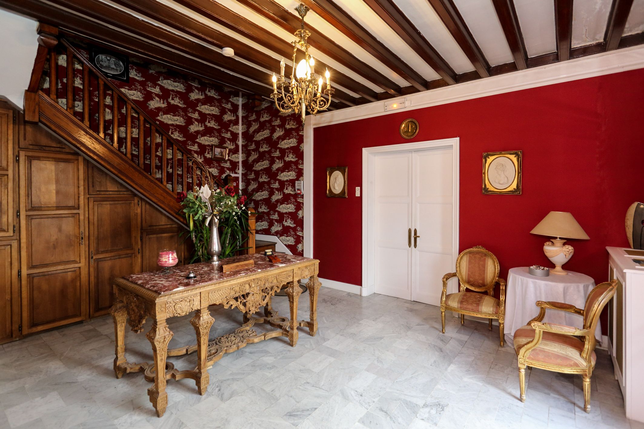 Ein Zimmer mit einer Holztreppe, einem Tisch mit einer Vase, zwei Stühlen und einer Kristallleuchter.