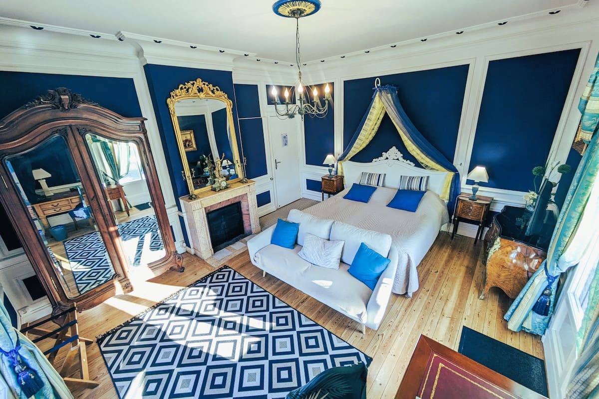 Ein Schlafzimmer mit einem großen Bett, einem Spiegel, einem Kamin und einer Kristallleuchter.