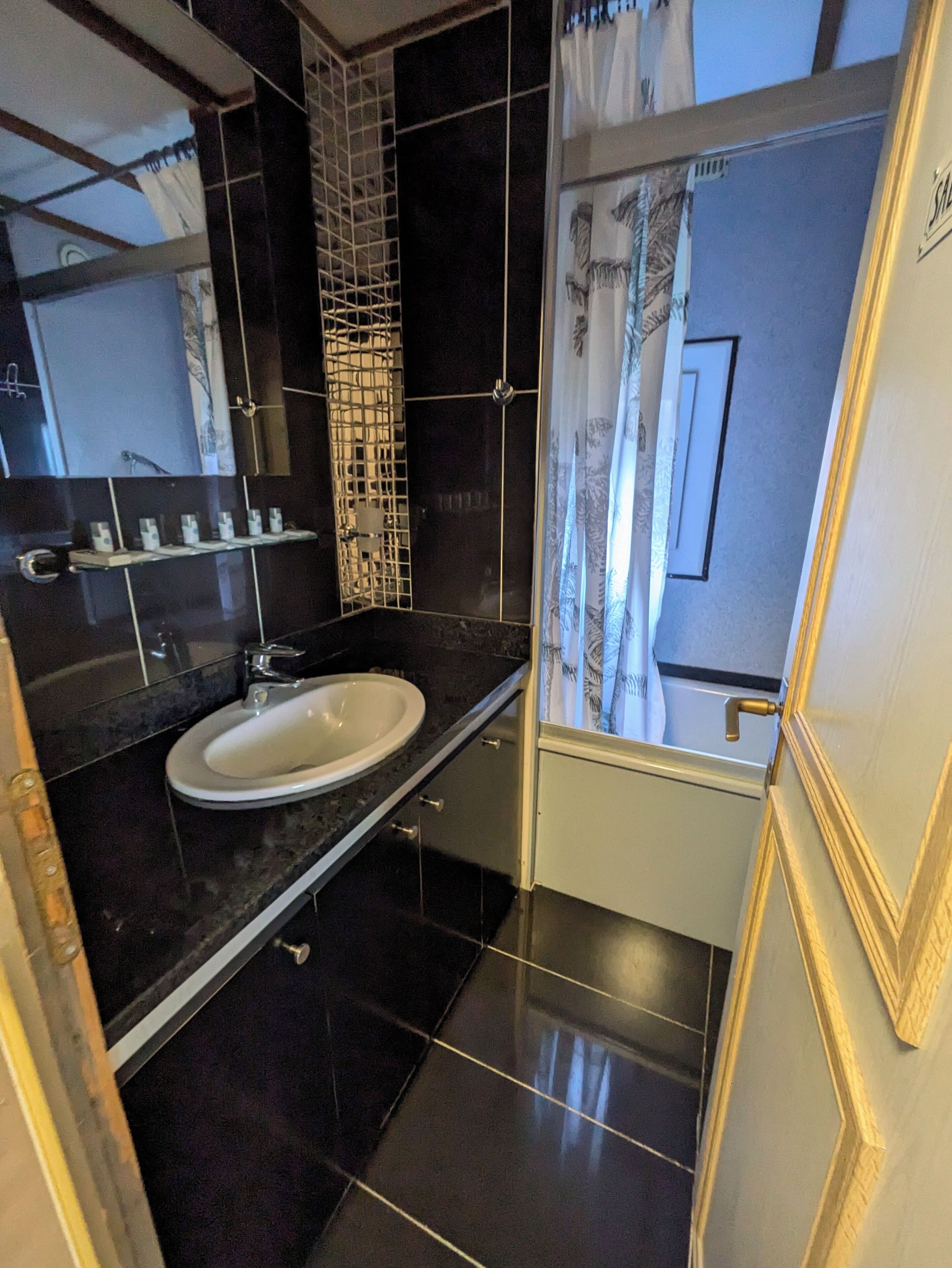 Un bany modern amb terra de rajoles negres, un lavabo blanc i una cabina de dutxa de vidre.