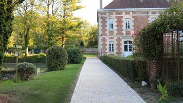 A paved pathway leading to a brick building with a garden and trees.