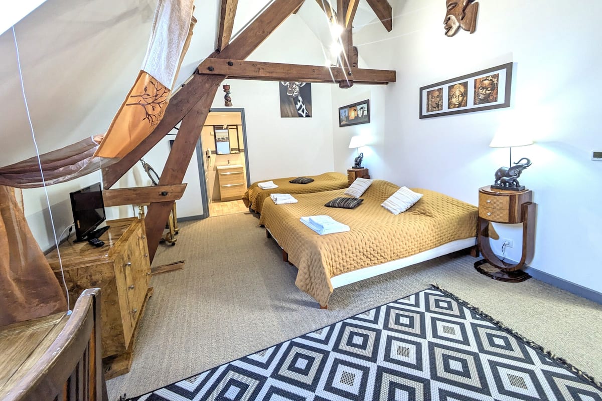 Ein Schlafzimmer mit einem großen Bett, Holzbalken, einem Schreibtisch, einem Stuhl, einem Fernseher und einem gemusterten Teppich.