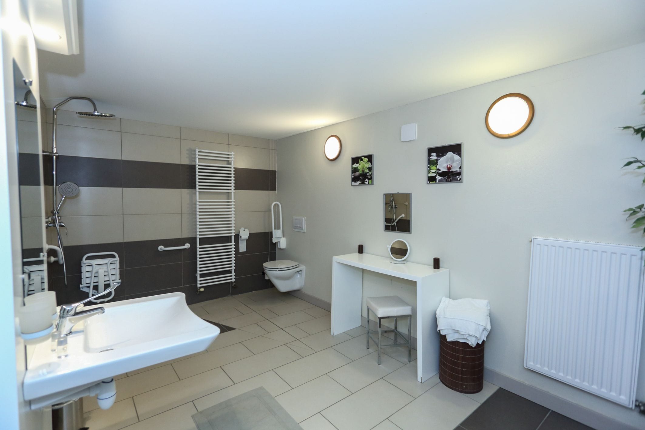 A modern bathroom with a sink, toilet, and shower. There is a white vanity with a mirror and a trash can.