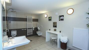 A modern bathroom with a sink, toilet, and shower. There is a white vanity with a mirror and a trash can.