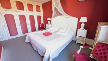A neatly arranged bedroom with a large bed, a red chair, a white nightstand, and a chandelier.