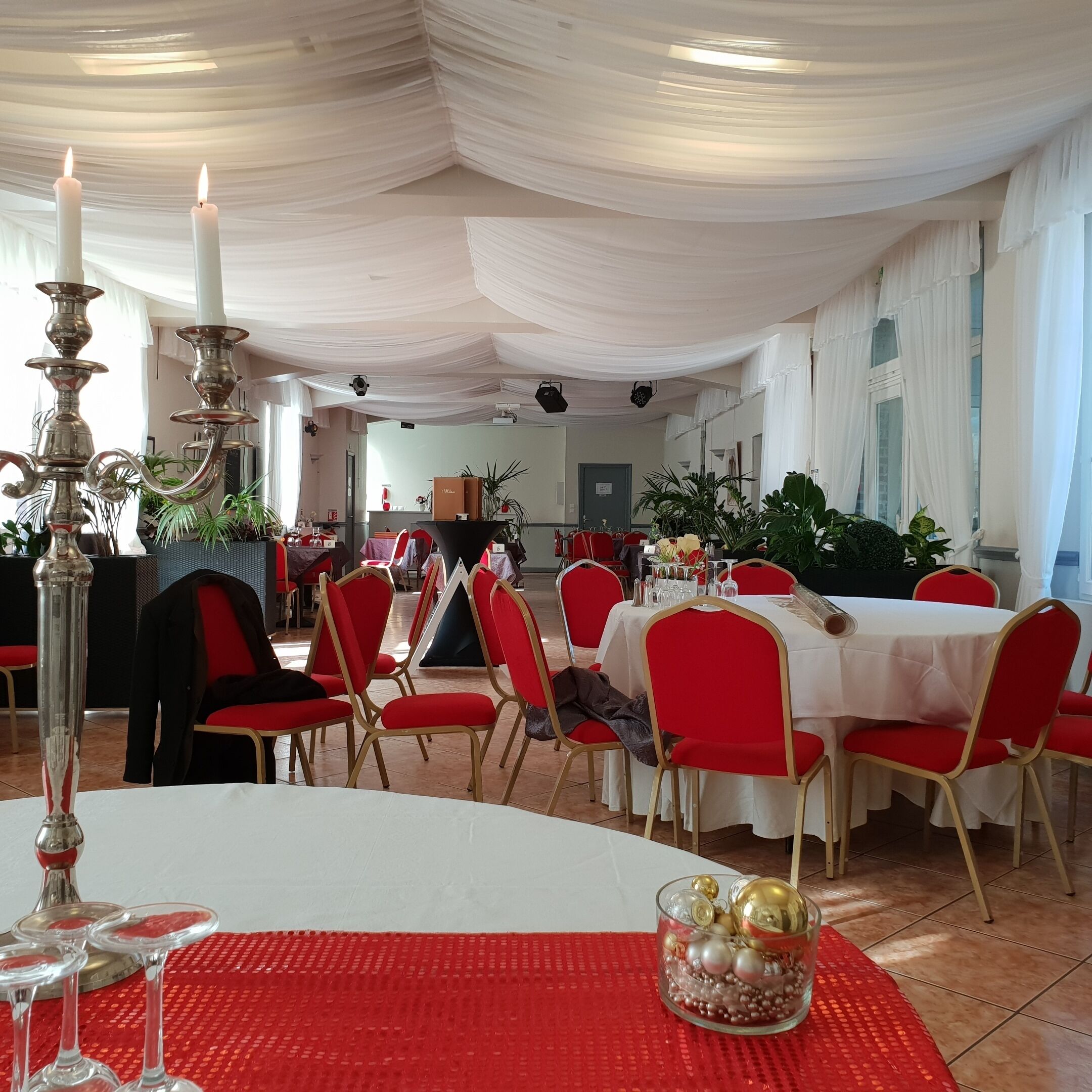 A banquet hall with round tables, red chairs, and white drapes.