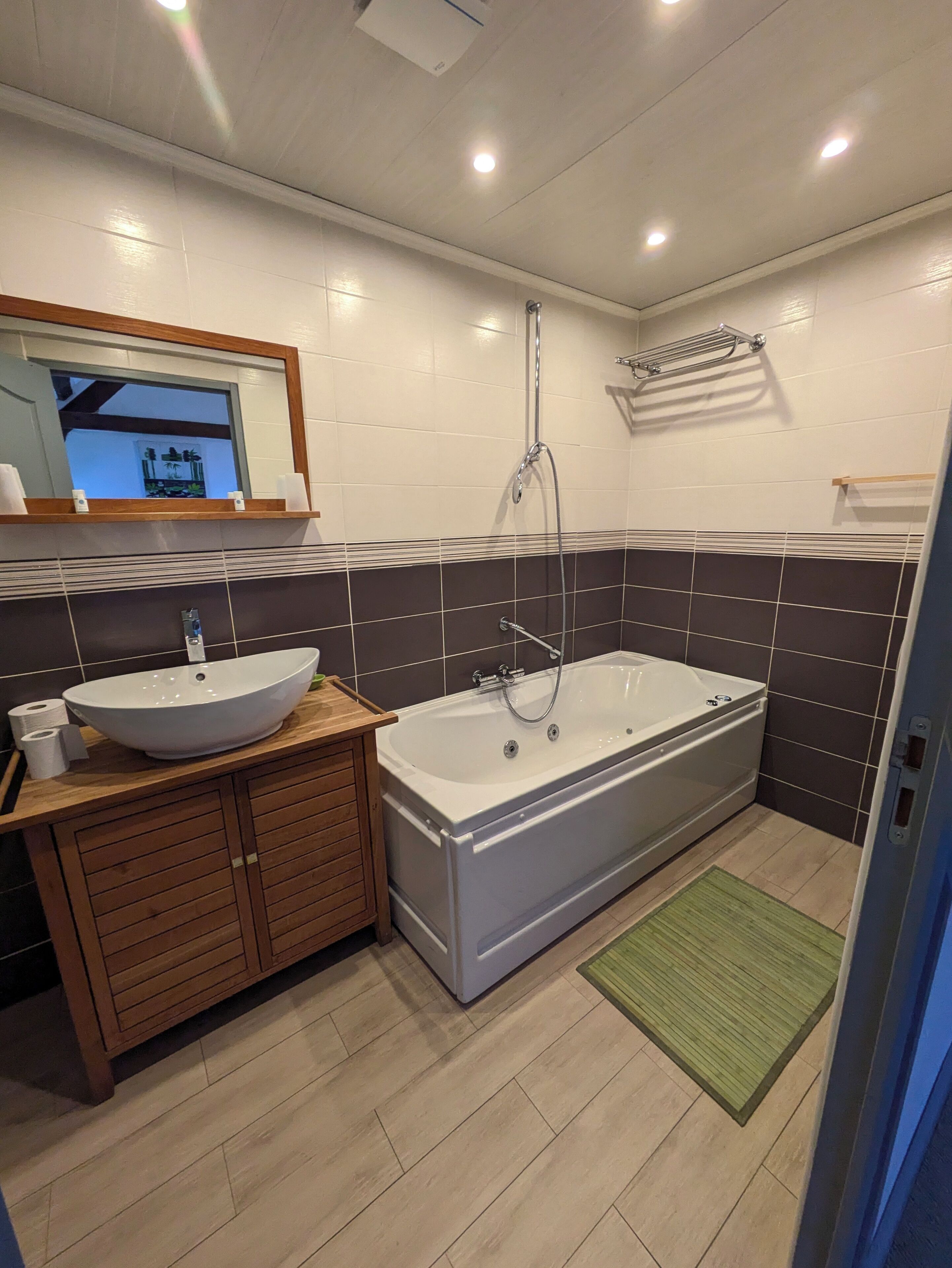 Un baño moderno con una bañera grande, un tocador de madera con un lavabo y un espejo sobre el tocador.