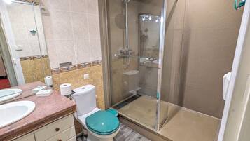 Un bany amb dutxa tancada amb vidre, un vàter amb seient color turquesa, un lavabo i un mirall.
