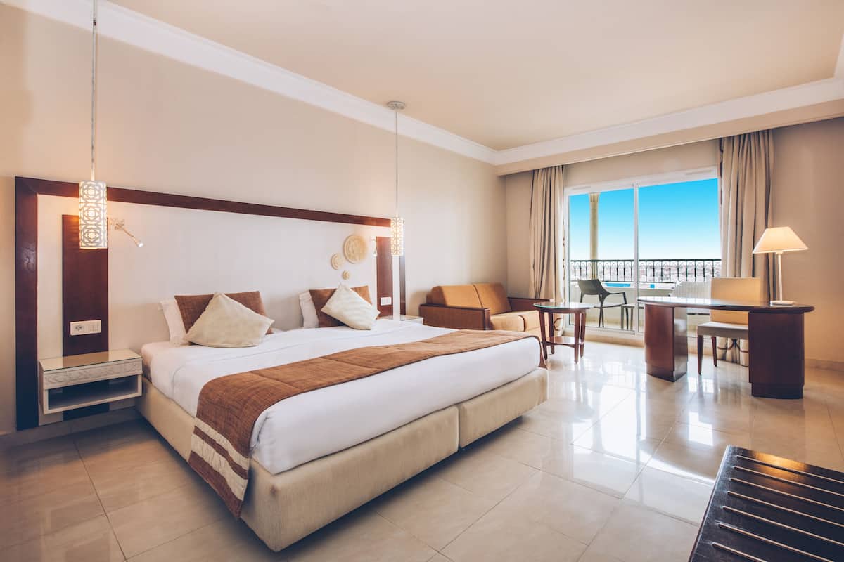 Habitación de hotel con una cama grande, un escritorio, una silla y un balcón con vistas.
