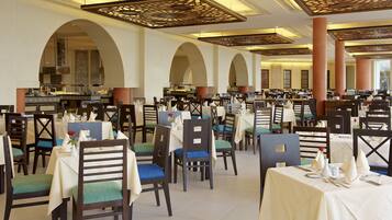 A spacious dining area with multiple tables and chairs, a central bar, and a high ceiling with decorative beams.