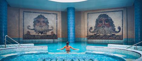 Una gran piscina interior con mosaicos y dos grandes murales en las paredes.