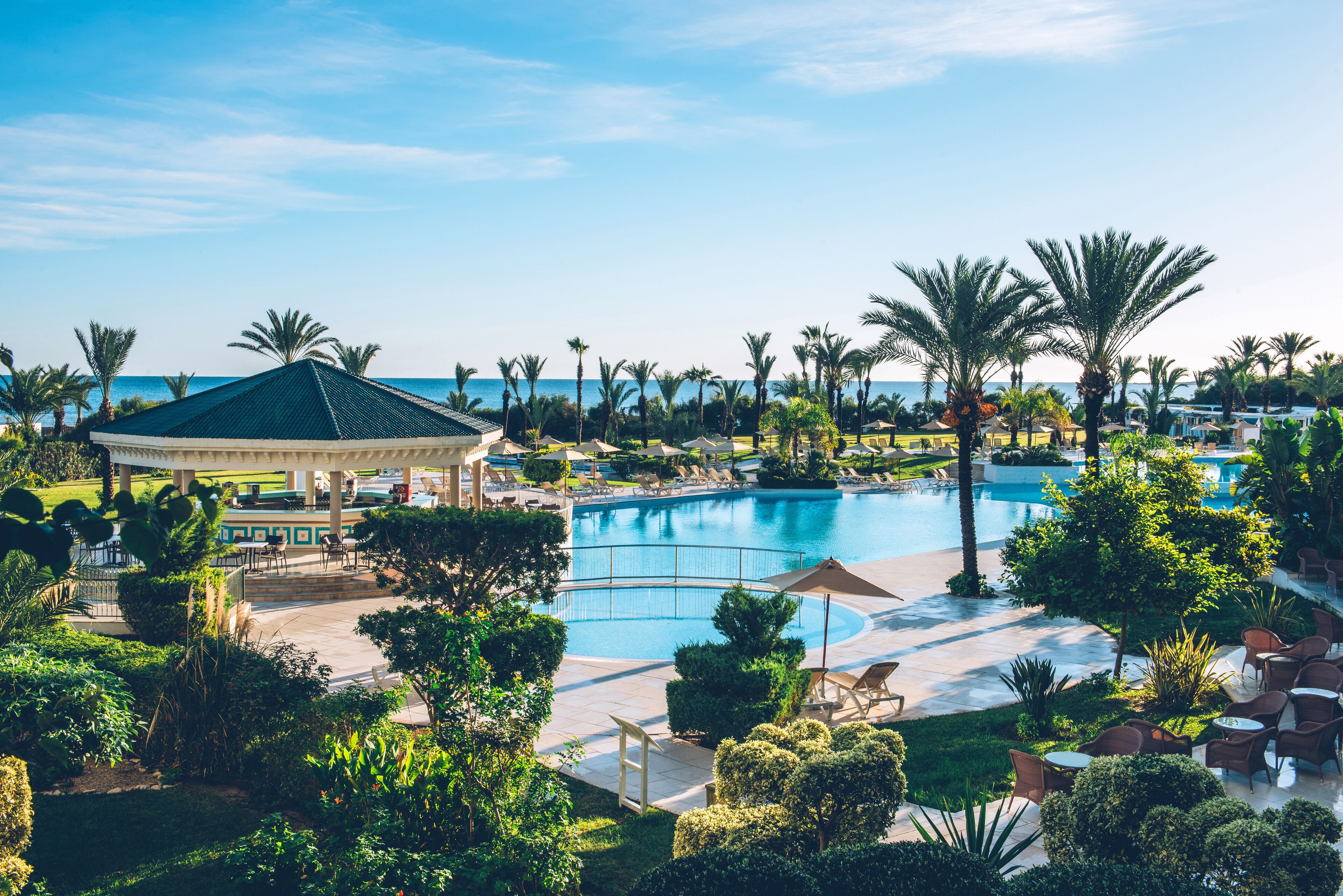Un resort con una piscina grande, palmeras y un pabellón.