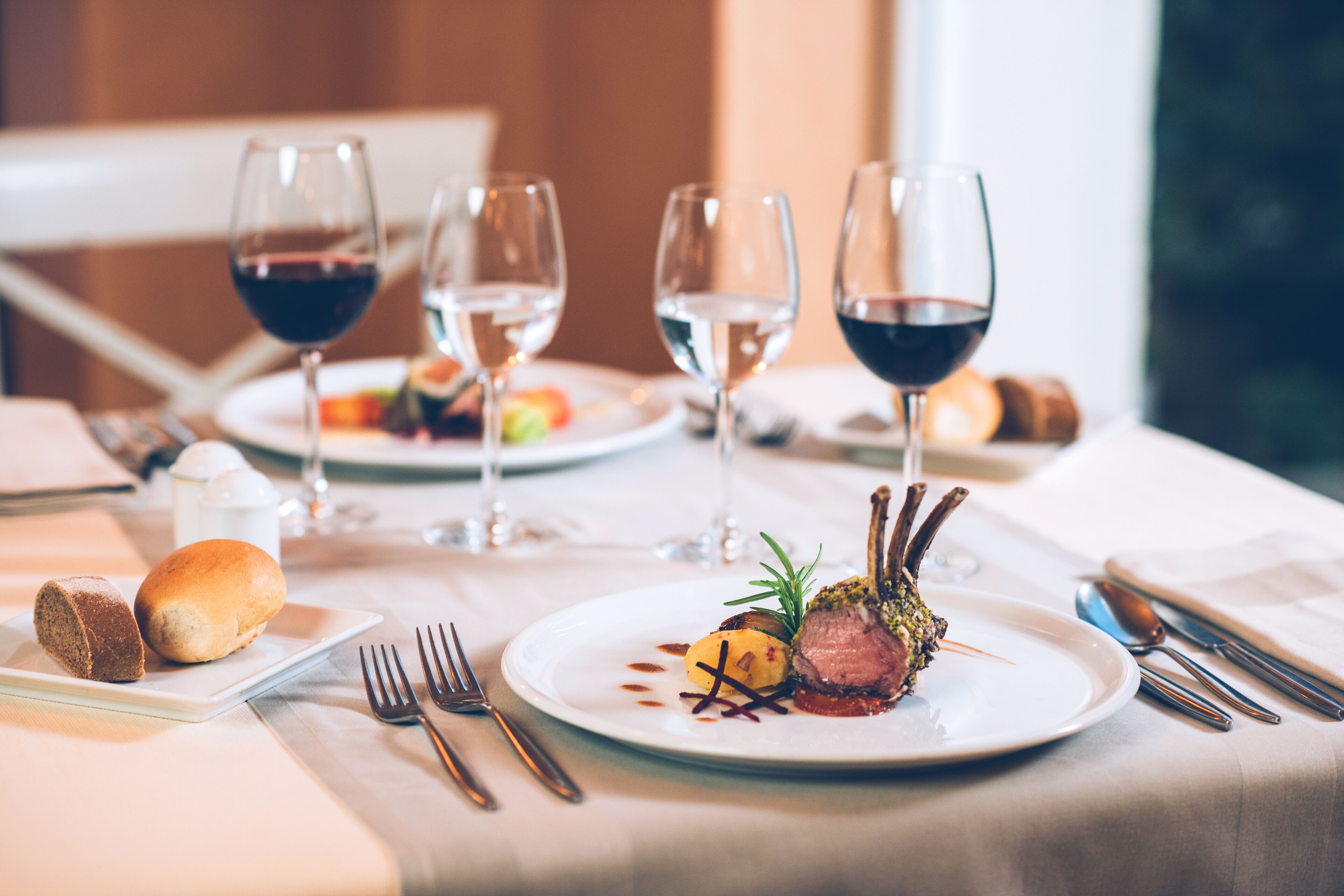 Una mesa de comedor con platos de comida, copas de vino y cubiertos.