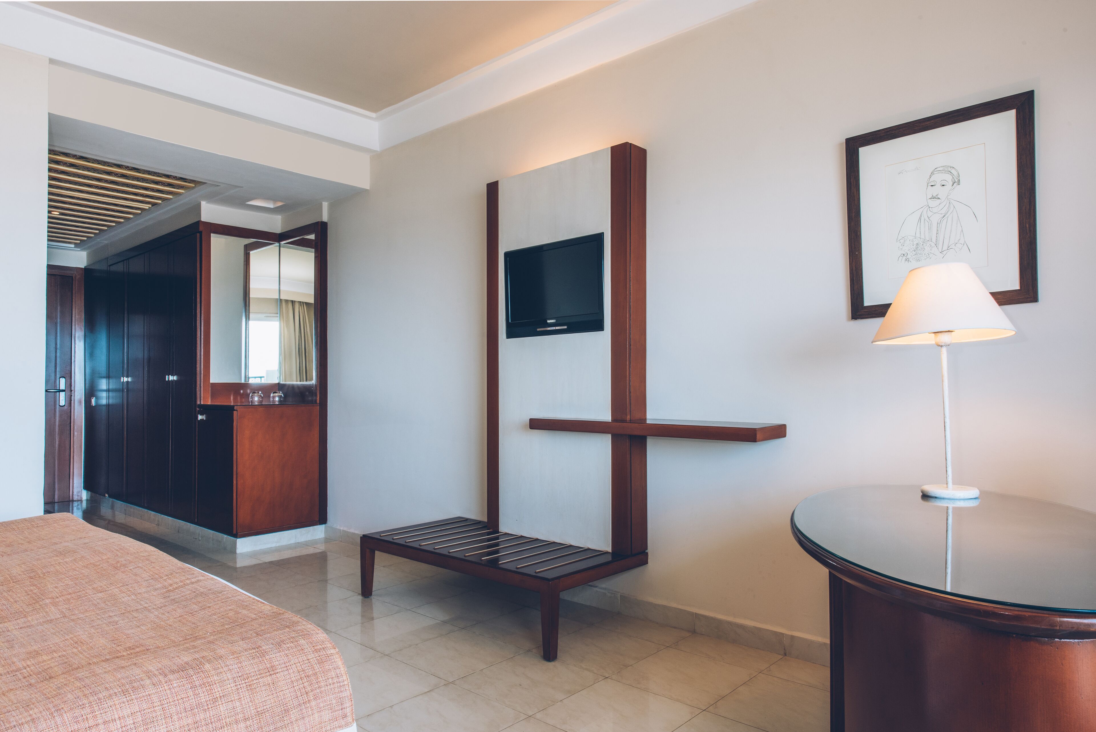 Habitación de hotel con cama, escritorio, silla, televisión montada en la pared y un cuadro enmarcado.