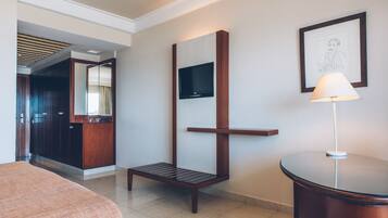 Habitación de hotel con cama, escritorio, silla, televisión montada en la pared y un cuadro enmarcado.