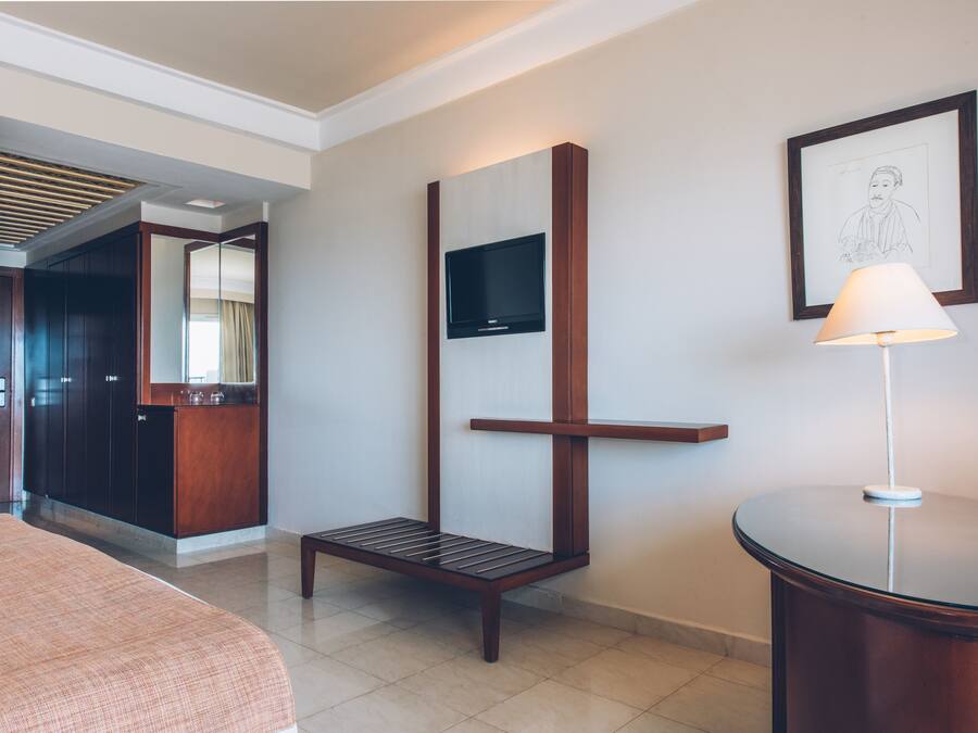 Habitación de hotel con cama, escritorio, silla, televisión montada en la pared y un cuadro enmarcado.