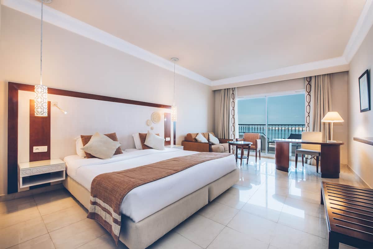 Una habitación de hotel con una cama grande, un escritorio, una silla, un balcón con vistas y una lámpara colgante.