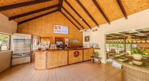 Zona de recepción con techo de madera, mostrador de recepción, refrigerador y vistas al exterior.