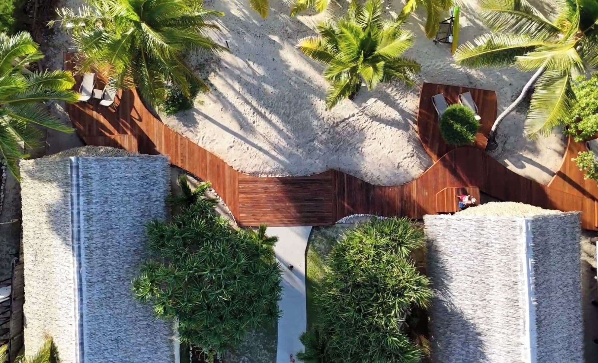 An aerial view of a resort with a wooden deck, palm trees, and lounge chairs.