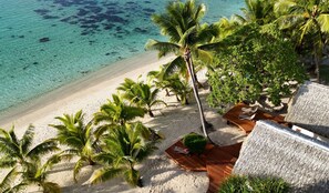 A beach with clear turquoise water, palm trees, and wooden deck seating. - Tamanu Beach (Aitutaki)