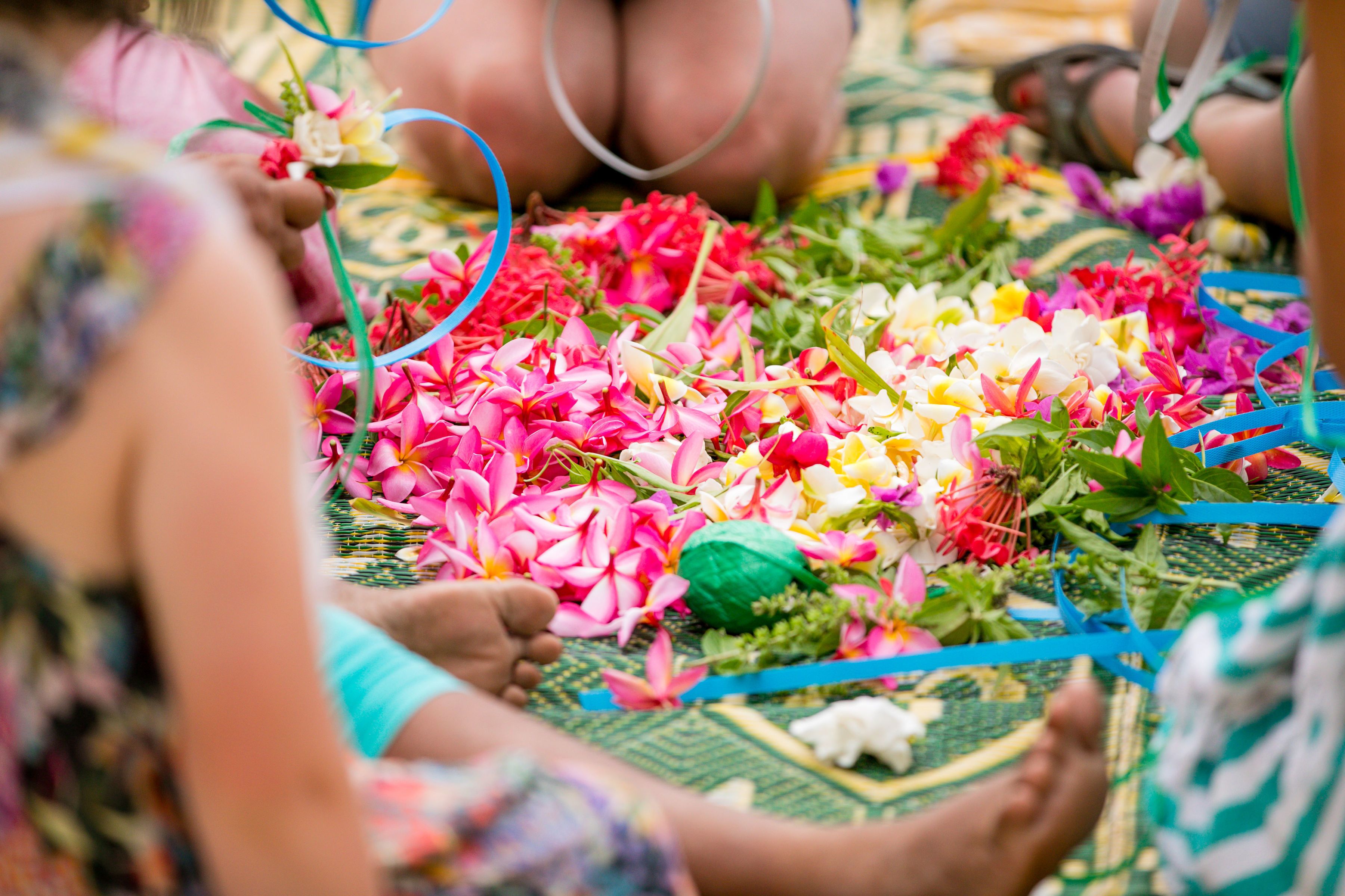 Un grupo de personas sentadas sobre una estera con motivos florales y listones de colores.