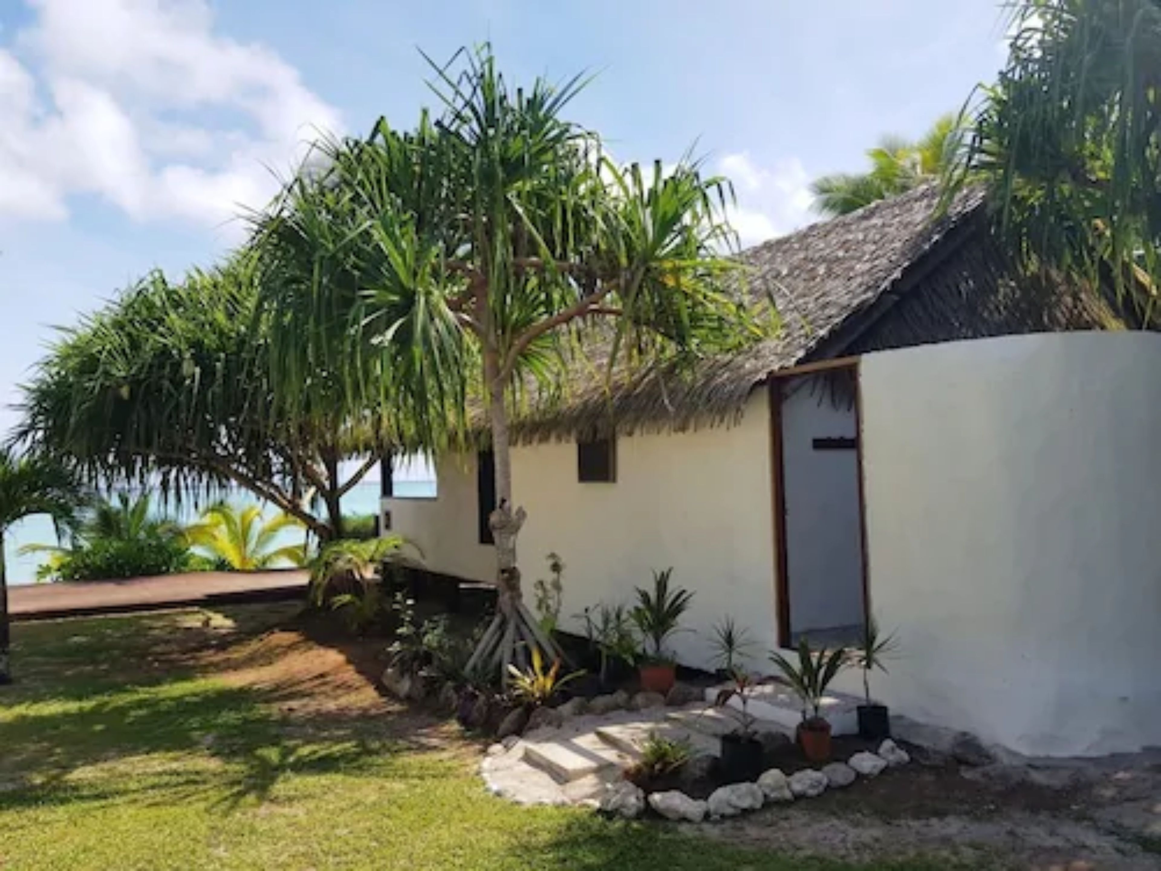A small, single-story building with a thatched roof, surrounded by tropical vegetation and a well-maintained lawn.