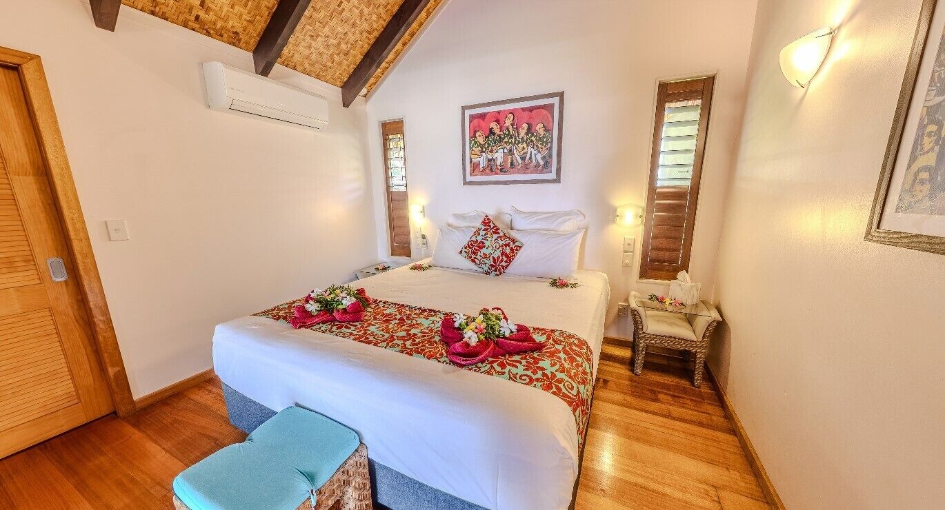 Una habitación de hotel con cama, una mesita, un banco y aire acondicionado instalado en la pared.