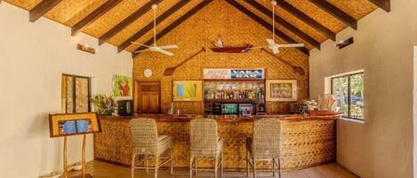 Zona de bar con techo alto, vigas de madera y barra con sillas.