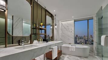 A modern bathroom with a large mirror, two sinks, a bathtub, and a city view.