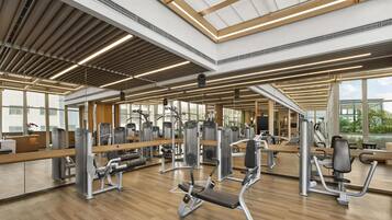 A spacious gym with various exercise machines, large windows, and a wooden floor.