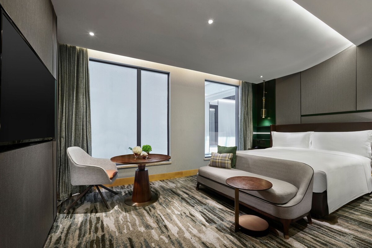 A modern hotel room with a large bed, a sofa, a small table, and a chair.