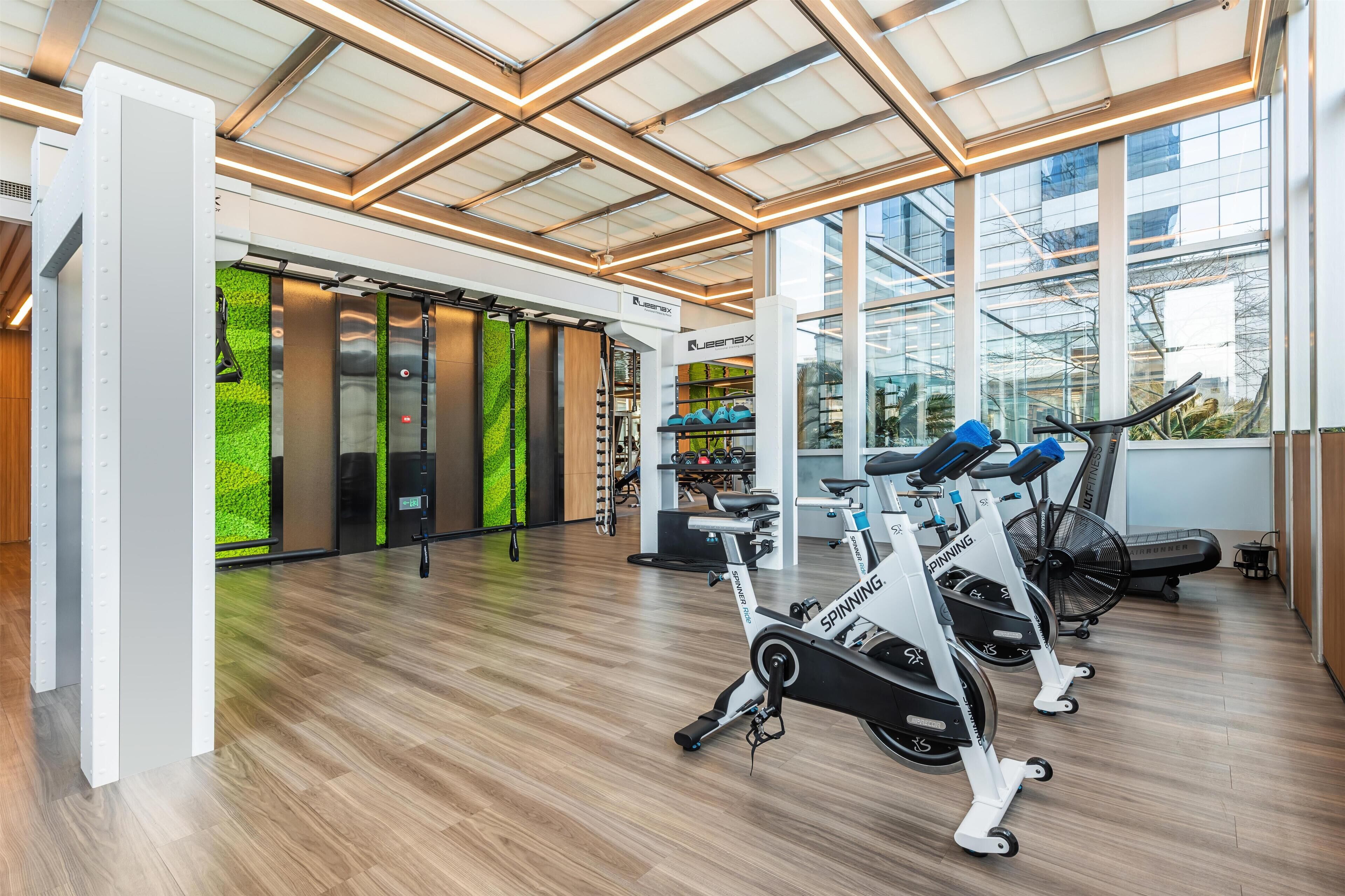A modern gym with exercise bikes, a green wall, and large windows.