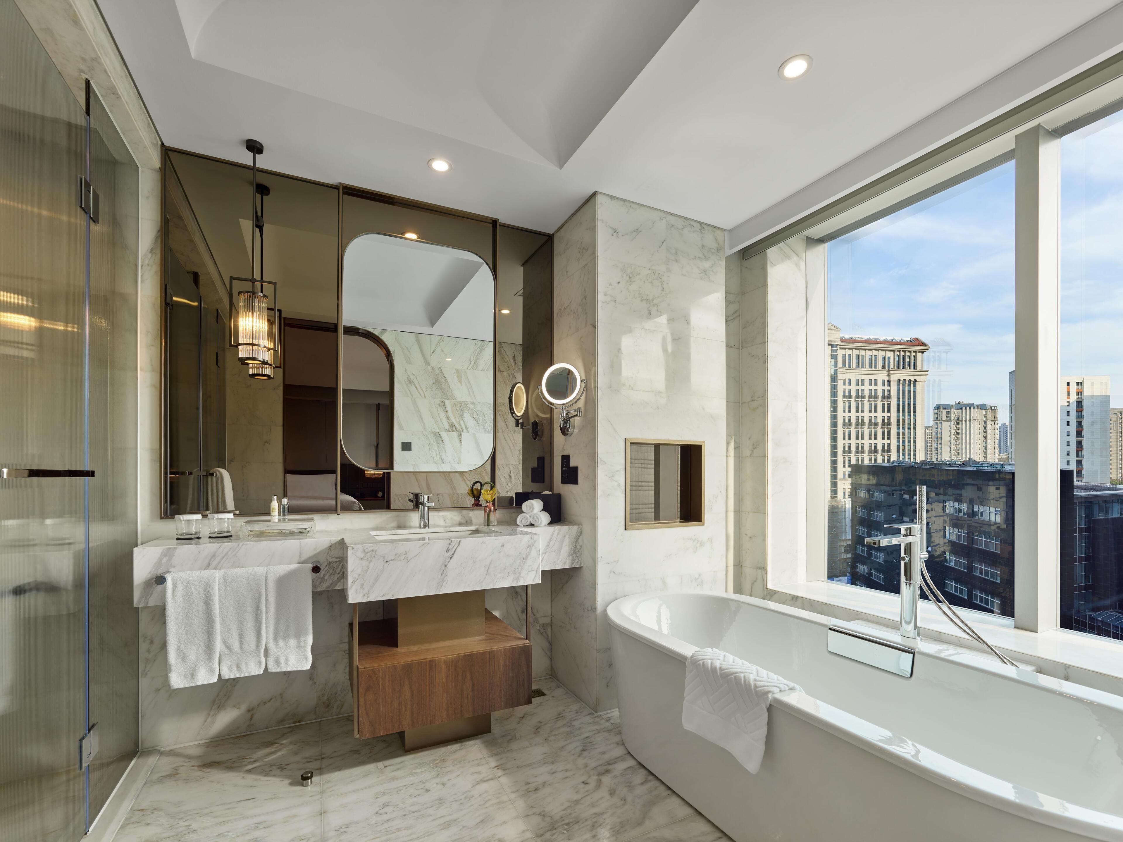 A modern bathroom with two sinks, a large mirror, a bathtub, and a view of the city.