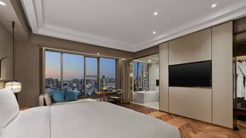 Una habitación de hotel moderna con una cama grande, una zona de comedor, un televisor y vistas a la ciudad.