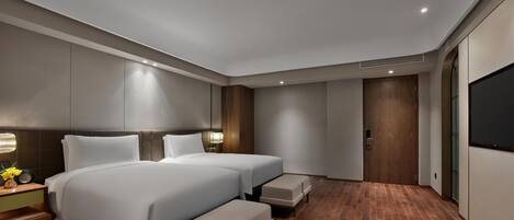 A modern hotel room with two beds, a TV, and a wooden floor.