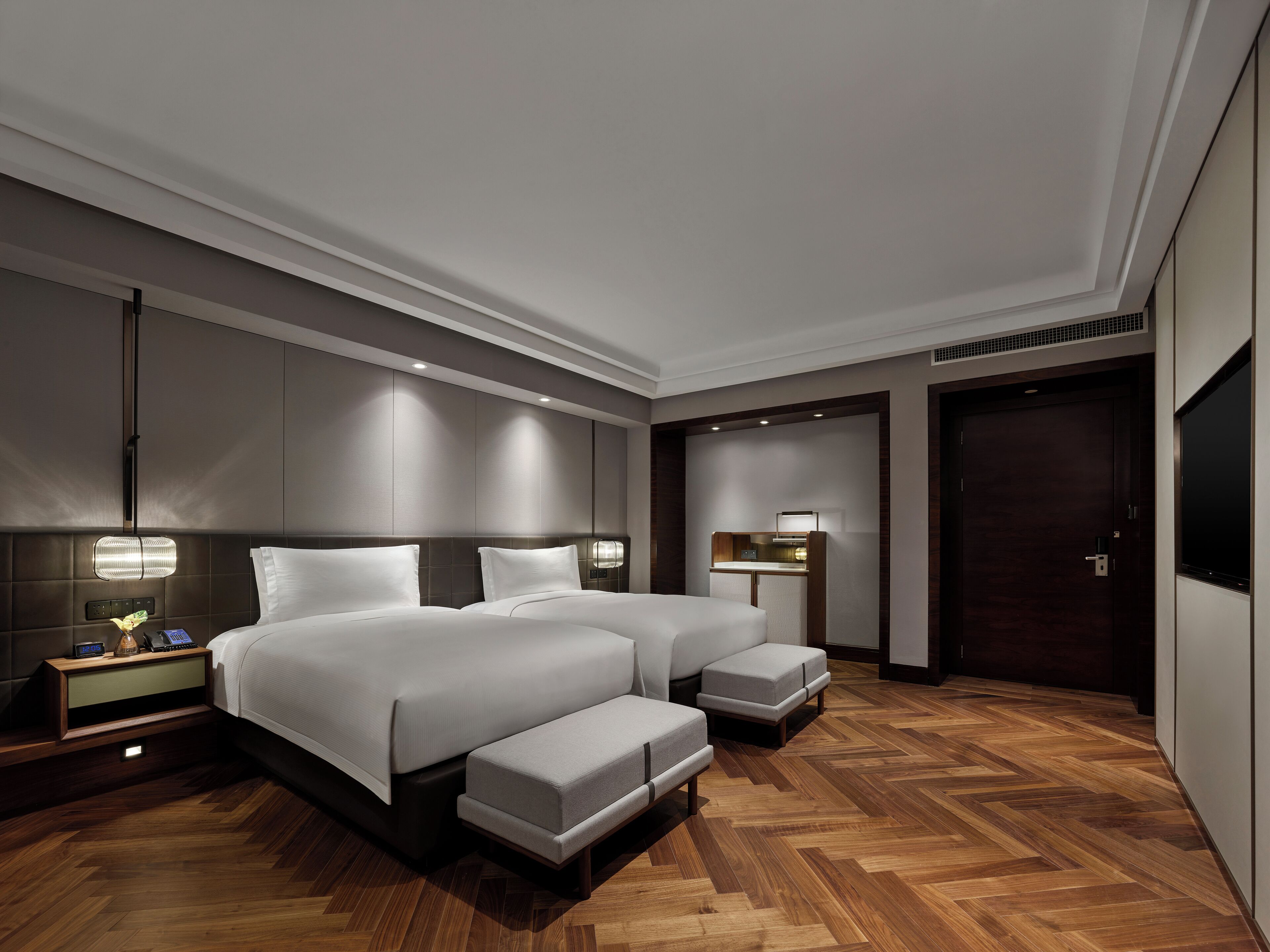 A modern hotel room with two beds, a desk, and a large wardrobe.