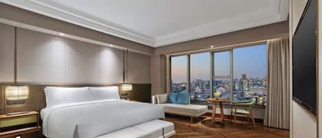 Una habitación de hotel moderna con una cama grande, un área de estar, una mesa de comedor y vistas a la ciudad.